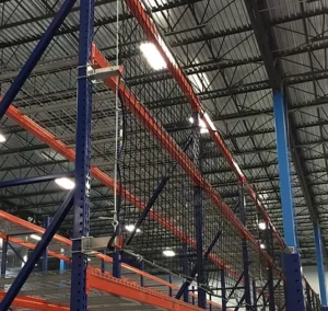 Industrial warehouse racking system with safety netting installed, viewed from below under a metal roof with overhead lighting—an ideal example of smart Warehouse Solutions for enhanced safety and efficiency.