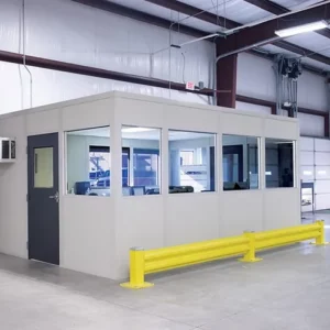 A modular office with large windows and a dark door is inside a warehouse; a yellow safety barrier is positioned in front, showcasing smart Warehouse Solutions.