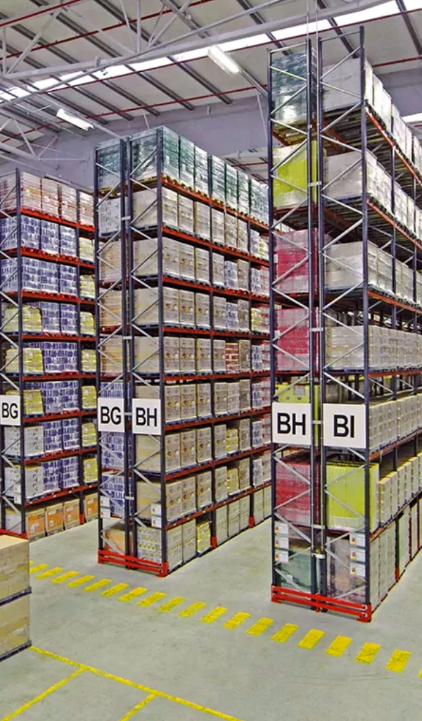 Tall metal shelves in a warehouse filled with organized boxes; each row of the Warehouse Storage Rack Systems is labeled with large signs, including "BG," "BH," and "BI.