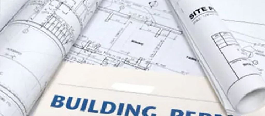 Rolled-up architectural blueprints and a document labeled "BUILDING PER" are displayed on a flat surface, reflecting the planning phase of Turnkey Warehouse Projects.