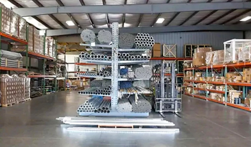 Metal pipes are stacked on a multi-level rack in a warehouse, showcasing the organized storage solutions used across the various Industries We Serve, with shelves of boxes and materials visible in the background.