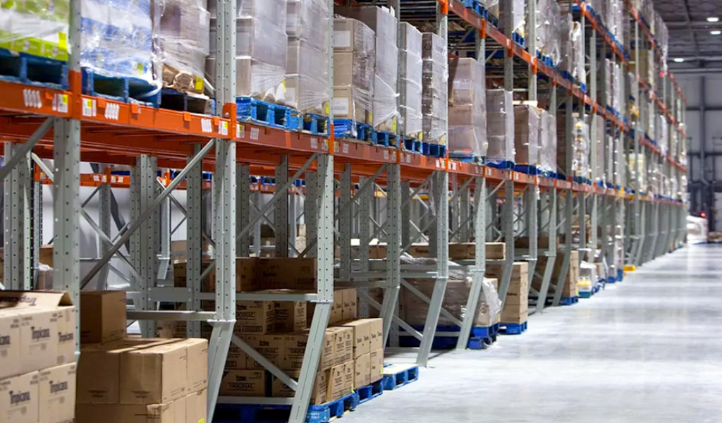 Warehouse interior with tall metal shelves storing stacked boxes and goods, organized on pallets, lining a wide concrete aisle—exemplifying the efficient storage solutions for the diverse Industries We Serve.