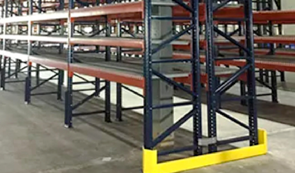 Industrial warehouse racking system with metal beams and yellow Industrial Warehouse Safety Guarding at the base, situated on a concrete floor.