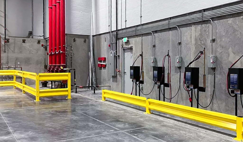 Industrial facility interior featuring exposed pipes, electrical panels mounted on a concrete wall, and Industrial Warehouse Safety Guarding with yellow safety barriers on a polished floor.