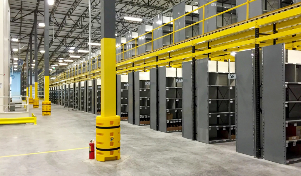 Rows of empty industrial warehouse shelves feature prominent yellow safety barriers and a fire extinguisher in the foreground, highlighting effective industrial warehouse safety guarding measures.