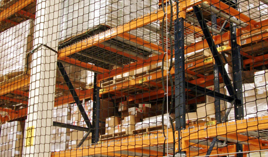 Industrial warehouse shelving with stacked boxes and pallets, secured by warehouse safety netting to ensure safety and protection.