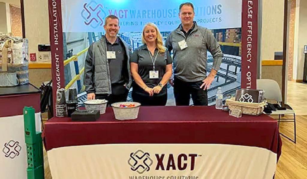 A group of people standing in front of a table, representing About Xact Warehouse Solutions.