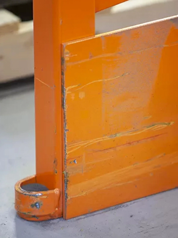 Close-up of an orange metal object with visible scratches, resting on a gray floor and partially inserted into a rounded metal bracket at the base—ideal for demonstrating the use of Rack Repair Kits.