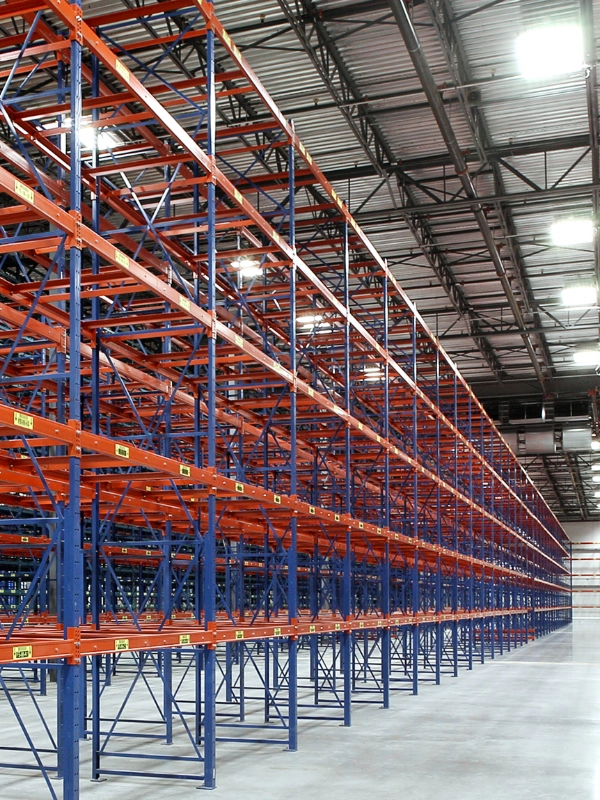 Rows of empty industrial warehouse shelving units made of blue and orange metal stand inside a large, well-lit facility, ready for installation or maintenance with Rack Repair Kits.