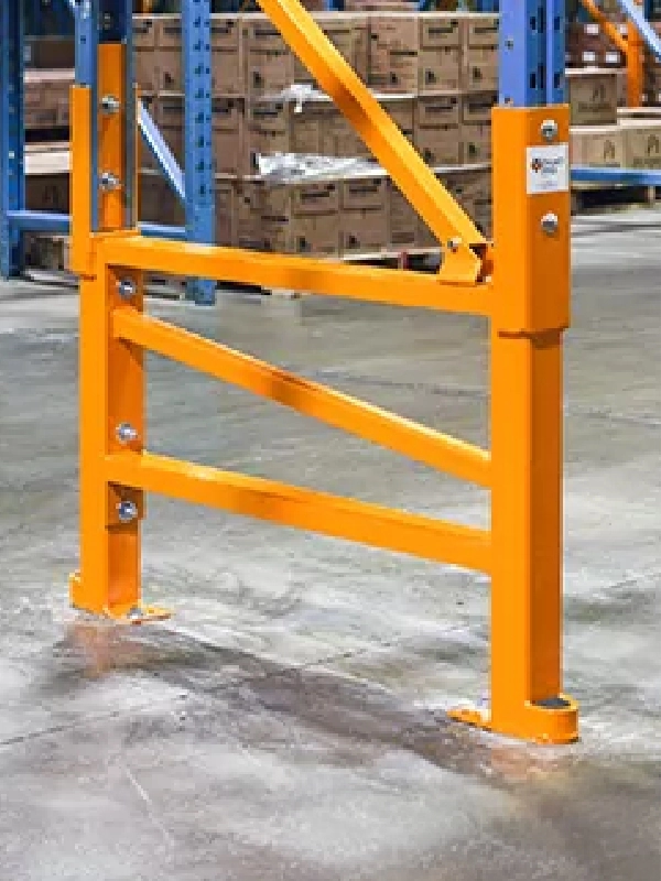 A yellow metal rack guard is bolted to a warehouse floor, offering extra protection alongside Rack Repair Kits for the base of a blue pallet racking system with boxes stacked in the background.
