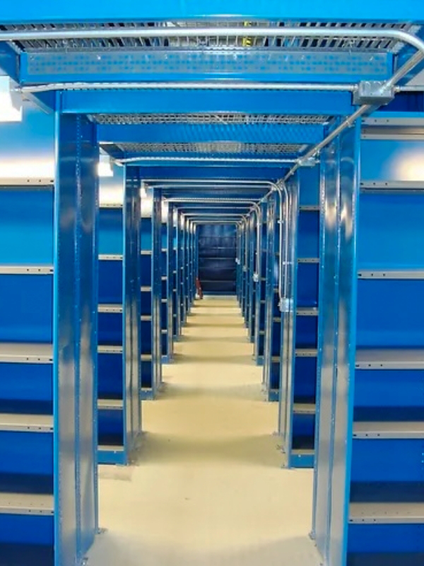 A perspective view of empty industrial shelving units lined up in rows with a blue background inside a warehouse or storage facility.