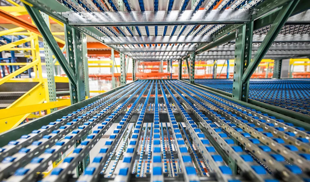 Close-up view of empty metal roller shelves in an industrial Carton Flow warehouse storage system, with rows of yellow, orange, and green structural beams.
