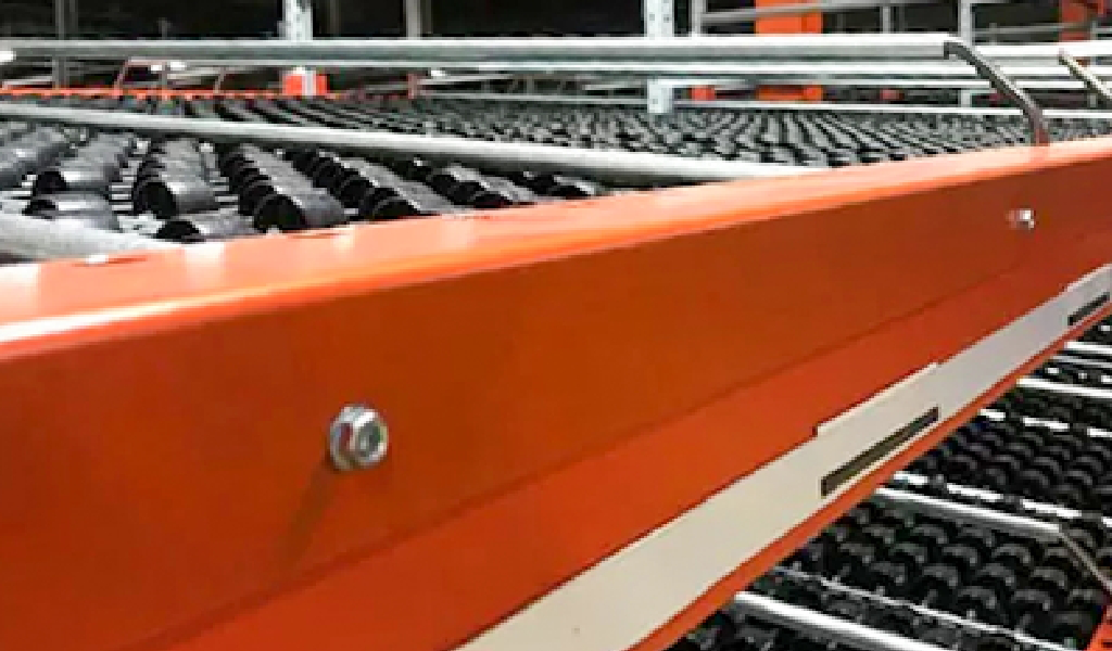 Close-up view of an orange industrial conveyor system with black roller tracks and metal rails, featuring a Carton Flow design for efficient material handling in a warehouse.