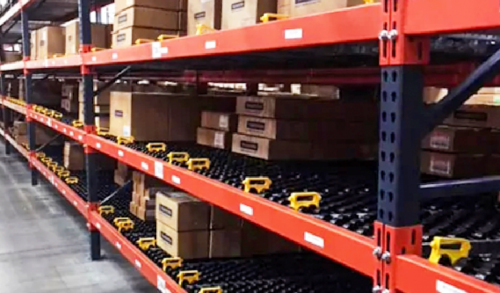 Brown cardboard boxes are stacked on red metal warehouse shelves equipped with black roller tracks, creating a carton flow system for efficient item movement.