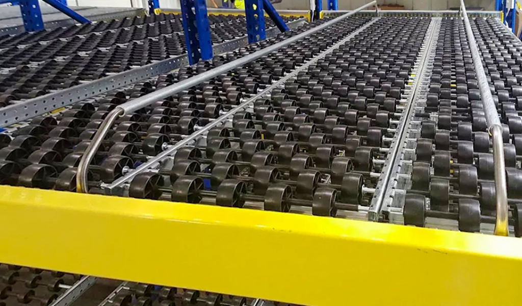 Close-up view of a carton flow roller conveyor system with multiple black rollers and blue and yellow metal frames, designed for efficient material handling in a warehouse or industrial setting.