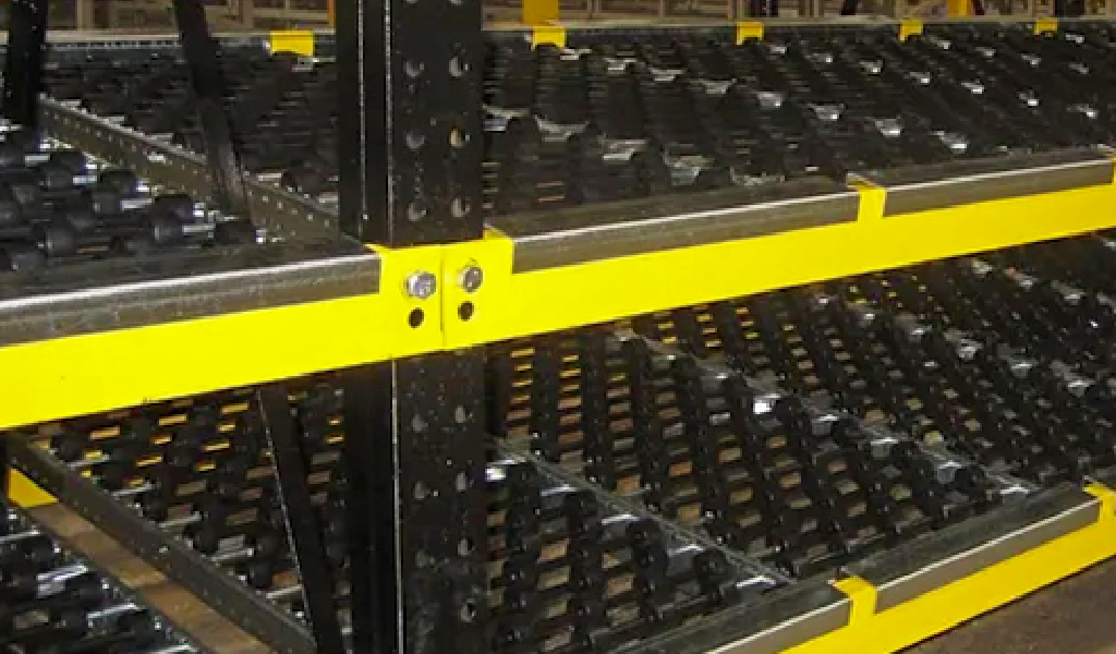 Close-up of industrial warehouse shelving with black metal rollers and yellow safety bars, featuring a Carton Flow design for moving and storing goods efficiently.